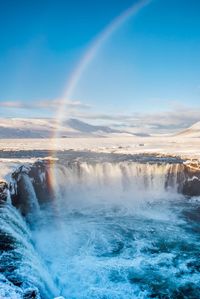 Scenic view of rainbow over waterfall against sky