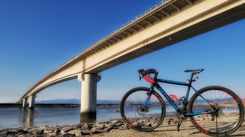 Bicycle by bridge against clear blue sky