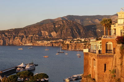 High angle view of boats moored at sea by historic building against mountains