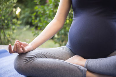 Low section of pregnant woman meditating at park