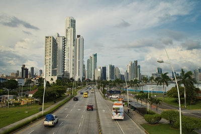 Vehicles on road by buildings in city against sky