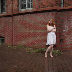 Thoughtful young woman embracing herself while standing against building