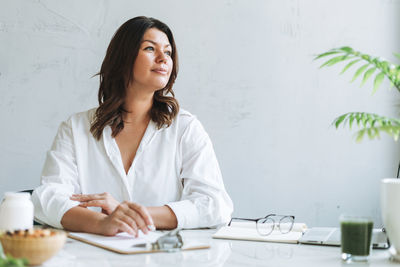 Young smiling brunette woman nutritionist plus size in white shirt working at laptop on table 