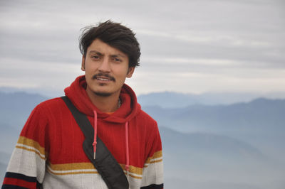 Closeup of a handsome young guy looking at camera while standing against the background of mountains 