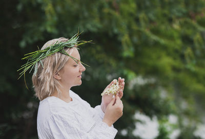 Woman in nightgown with wreath holds elderberry flowers in the forest