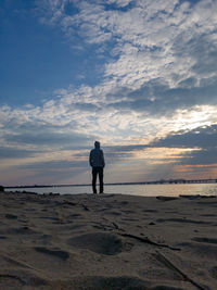 Rear view of man standing on beach against sky during sunset