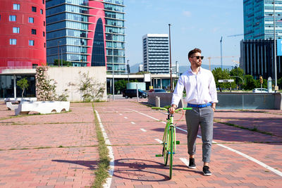 Bearded man in sunglasses walking with bike by bicycle track outdoors