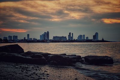 Sea by buildings against sky during sunset