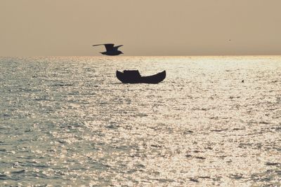 Silhouette bird flying over sea against sky