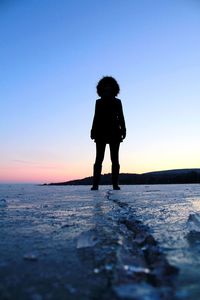 Surface level of silhouette woman standing at beach against sky during sunset