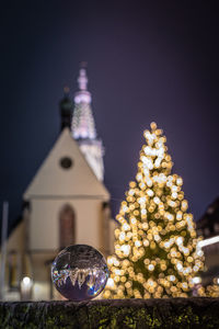 Illuminated christmas tree by building against sky at night