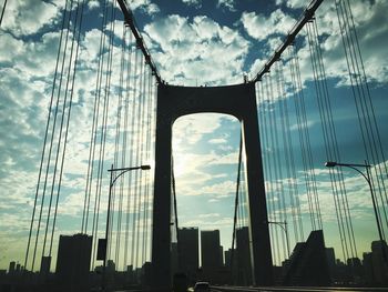 Low angle view of suspension bridge against cloudy sky