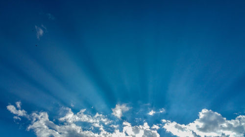 Low angle view of clouds and sunrays in blue sky