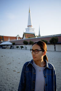 Young woman looking away while standing against sky