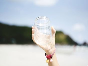 Close-up of hand holding glass against water