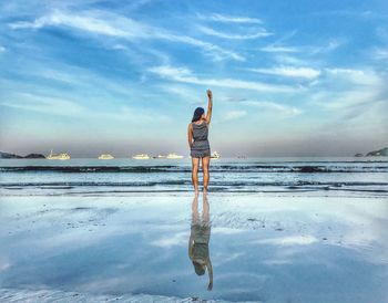 Rear view of woman standing on beach against sky