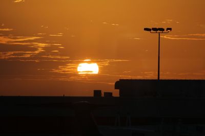 Silhouette street by sea against orange sky