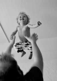 Low angle view of playful father catching baby boy in mid-air at home