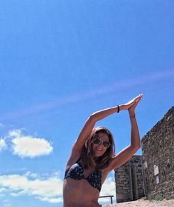Low angle view of young woman practicing yoga against blue sky on sunny day
