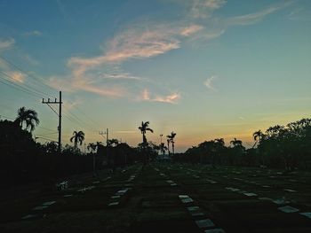 Road by trees against sky during sunset