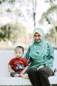 Portrait of smiling mother with son sitting on bench at park