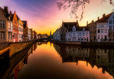 Reflection of buildings on river against sky during sunset