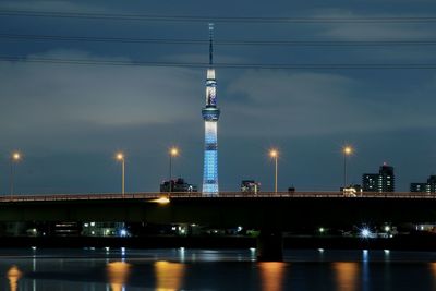 Illuminated bridge over river by buildings against sky at night