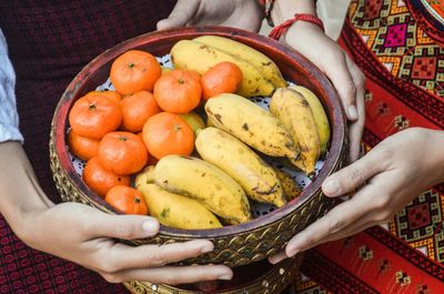 Midsection of thai women holding fruits in wooden bowl as an offering to buddha