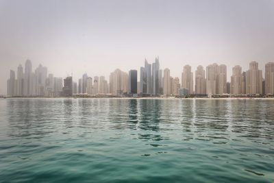 Sea by buildings in city against sky