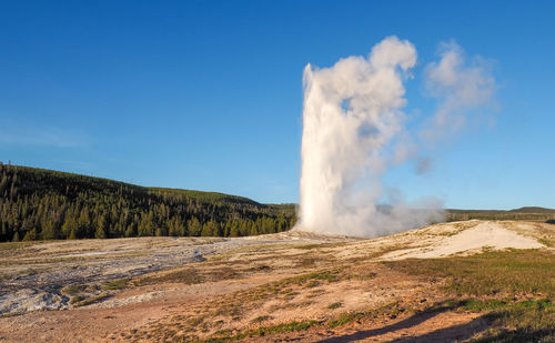 Old faithful geyser erupting on a sunny day with blue sky. yellowstone national park