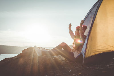 Woman sitting by tent on mountain against sky