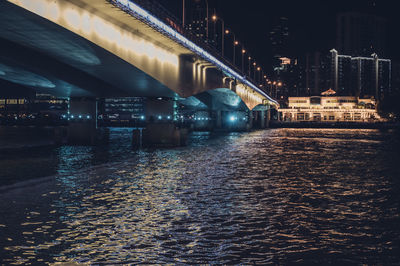 Illuminated bridge over river by buildings in city at night