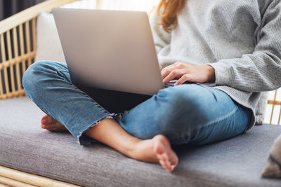 Low section of woman using laptop while sitting on sofa at home