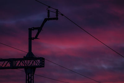 Low angle view of silhouette electricity pylon against dramatic sky