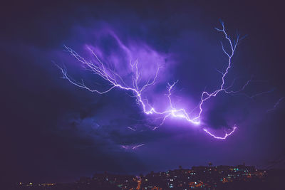 Low angle view of lightning over city at night