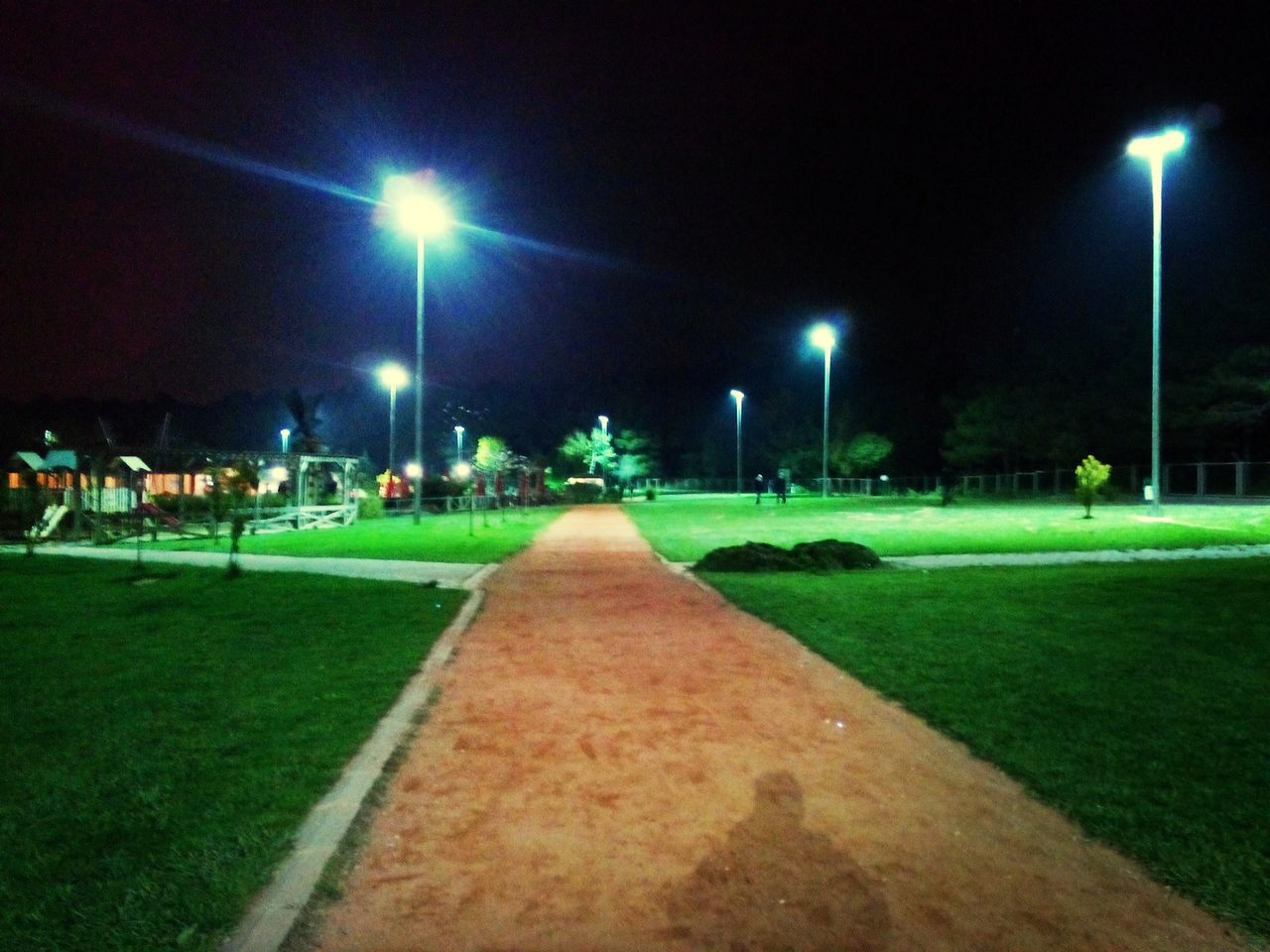 illuminated, night, street light, lighting equipment, grass, the way forward, green color, diminishing perspective, footpath, empty, building exterior, built structure, lamp post, road, outdoors, vanishing point, street, architecture, incidental people, sky