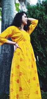 Young woman looking away while standing against yellow tree