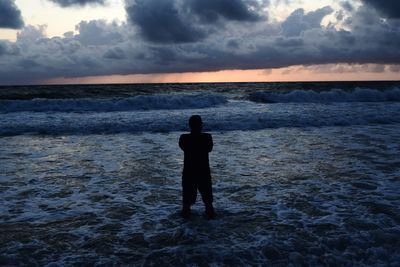 Rear view of man standing on beach during sunset