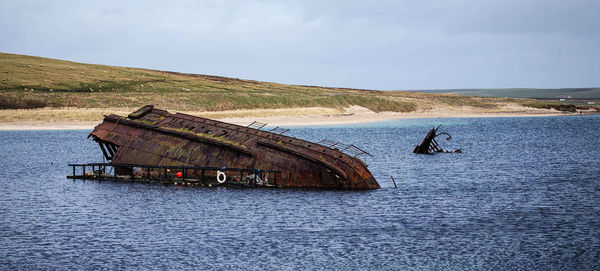 Abandoned boat on sea shore against sky