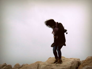 Full length of woman standing on rock against sky during windy day