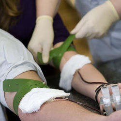 Midsection of nurse tying belt on patient hand in hospital