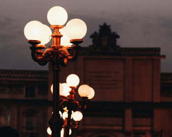 Illuminated lamp posts against building at dusk