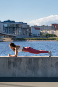 Fit young athletic woman in pink legging doing plank exercise working on abdominal muscles.