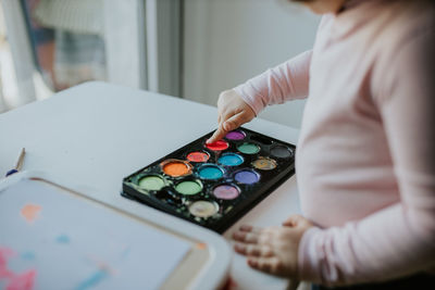 Midsection of girl touching paint in palette