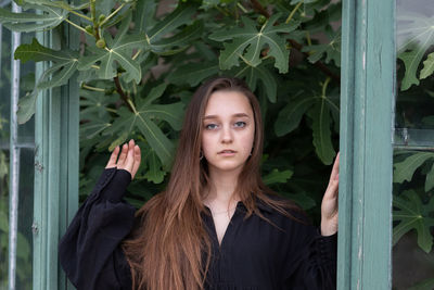 Portrait of young woman standing by gate against plants