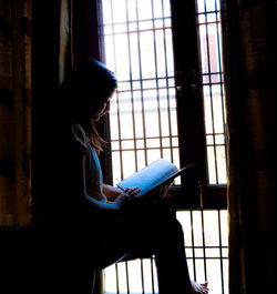 Side view of young woman sitting by window