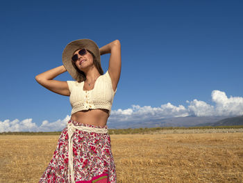 Young woman standing on field against sky