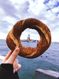 Cropped hand of woman holding baked pastry item against sea