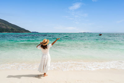 Rear view of woman standing at beach against sky