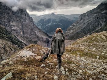 Rear view of man standing on rock against mountains